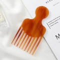 Detailed close-up of amber acetate wide tooth comb resting on elegant white silk fabric - Coffee