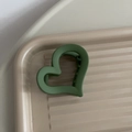 Dettaglio macro della molletta per capelli a cuore in verde opaco sul vassoio - Verde