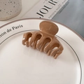 Glänzende Haarklammer in Karamellbraun auf einer minimalistischen Keramikschale - Braun