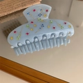 Detailed view of light blue acetate hair claw with colorful rhinestones on mirror surface - Blue