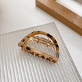 Close-up of amber tortoiseshell claw clip with gold metal spring on textured board - Beige Tortoise Shell