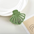 Detail view of a shell-shaped matte sage green hair claw clip on a ceramic plate - 7cm / Green