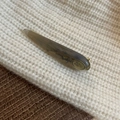 Detailaufnahme der Bernstein-Haarklammer mit Goldmetallbasis auf weißem Strickpullover - Graue Marmorstruktur