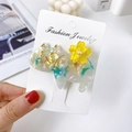 Detailed close-up of a marbled acetate cat hair clip with yellow flower held by hand - Iridescent Cyan
