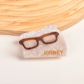 Detailansicht der Acetat-Haarklammer in Brillenform mit goldener JORNEY-Gravur am Rand - Cremefarbene Brille (7 cm Haarkralle)
