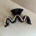 Gros plan sur une pince à cheveux noire ondulée ornée de strass brillants sur fond beige - Noir