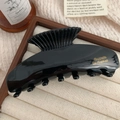Vista detallada de una pinza para el cabello de acetato negro con logo dorado en base de terciopelo - Negro