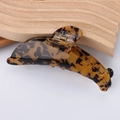 Detail view of a dolphin-shaped tortoiseshell hair claw clip on a light wooden wave stand - Dark Tortoiseshell Pattern