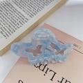 Detail of light blue acetate butterfly hair claw clip with elegant marble texture on a book - Blue