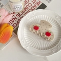 Detail of a creamy hair claw clip with red apple motifs and rhinestones on a porcelain plate - Beige Apple