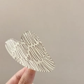 Detail view of a cream heart hair claw clip with brown wavy patterns held in hand - Approx. 7.3cm / Beige