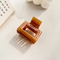 Detail of amber acetate hair claw clip with glossy finish on white leather background - 3.5cm / Tan