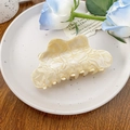 Close-up of a large cream marble acetate claw clip with wavy edges on a ceramic plate - 10.5cm / Off-white