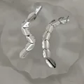Macro detail of silver oval tassel earrings with polished metallic fringe on white fabric - Silver