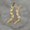 Macro view of gold-plated oval fringe drop earrings with polished mirror finish details - Gold