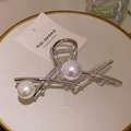 Detalle de pinza para el cabello en metal plateado con perlas sobre plato cerámico - Plateado