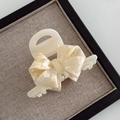 Macro view of a pearlescent white acetate hair claw clip with bow design and metal spring - 7.5cm / Cream