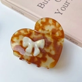 Detail of heart-shaped tortoiseshell hair claw with white pearlized bow on a book - Caramel