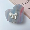 Close-up of heart-shaped acetate hair claw clip with colorful stripes and 3D bow accent - Textured White