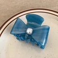 Detailed view of a blue acetate bow hair claw clip with a square faux pearl in a ceramic dish - 6cm / Blue