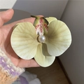 Vue détaillée d'une pince à cheveux orchidée jaune avec pétales réalistes et perle centrale - Jaune-vert