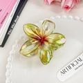 Macro shot of an iridescent yellow plumeria flower hair claw clip on a white plate - Apple Green