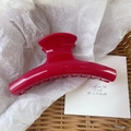 Top view of a large glossy red curved hair claw clip on white paper in a woven basket - 11.5x4.5cm / Bright Red