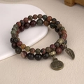 Detailed close-up of beaded bracelets set with tree of life and leaf charms in bronze - Picasso Jasper