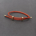 Detailed view of red braided steel rope bracelet with golden metal sliding clasps and tips - Red
