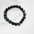 Dettaglio di perline in pietra lavica nera con distanziatori dorati su un piatto bianco - Stile Pietra Lavica Quadrata (10mm)