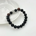 Dettaglio macro di un braccialetto di perle nere da uomo con accento argento su piatto bianco - Stile Occhio di Tigre Rosso Acciaio Inossidabile (10mm)