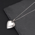 Primer plano de un relicario de plata en forma de corazón sobre fondo de piedra - Relicario Corazón Liso Acero