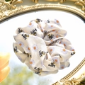 Detailstruktur eines beigen Haargummis mit Gänseblümchen- und Bienenmuster - Biene Gänseblümchen Druck Haargummi