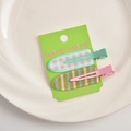Detail view of two colorful seamless duckbill hair clips with plaid and stripe patterns - Green Series