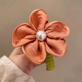 Dettaglio di una molletta per capelli a fiore in raso con perla e clip verde - Arancione