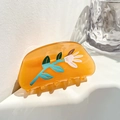 Close-up of orange floral acrylic hair claw clip with white flowers and green leaves - Floral / Orange