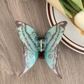 Détail d'une pince à cheveux papillon bleue avec ressort doré sur fond en bois - Motif Vert-Brun
