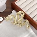 Close-up detail of a large gold snake-shaped metal hair claw clip with a polished finish - Gold Snake