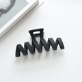Macro shot of matte black wavy claw clip on white surface with lifestyle accents - 11.3cm / Black