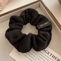 Close-up of black pleated hair scrunchie with knit texture and fabric care label - 10cm / Black