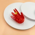 Nahaufnahme einer Haarklammer aus rotem Acetat in Handform mit einem gelben Ring-Detail - Stinkefinger-Geste