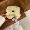 Detail eines beigen Haargummis mit fliederfarbenen Tulpenanhängern auf Holzregal - Gelb
