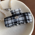 Detailed macro view of black and white checkered acetate hair claw with silver metal logo tag - 7cm