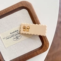 Detailopname van crèmekleurige golvende haarclip met gouden strik op houten dienblad - Crèmewit 5cm