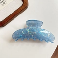 Detailed macro view of light blue acetate hair claw with mosaic glitter and gold branding - Blue Checkered