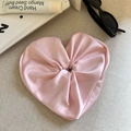 Detalle de un coletero de satén rosa en forma de corazón sobre tela beige texturizada - Rosa