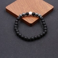 Dettaglio della cavigliera con perline nere opache e una perla centrale in ceramica bianca - Howlite