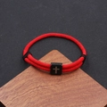 Detail of red woven rope bracelet with black stainless steel cross charm on wood - Red