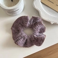 Dettaglio dello scrunchie in maglia lilla con bordi a balze marroni su tavolo bianco - Viola