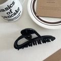 Close-up of a hollow black hair claw clip styled on a minimalist aesthetic table setting - Black 11.5cm